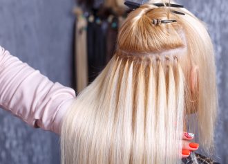 Hair extensions procedure. Hairdresser does hair extensions to young girl, blonde in a beauty salon